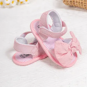 Close-up of pink baby sandals with floral embroidery, bow detail and velcro closure