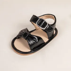 Detail of baby sandal featuring a black bow, silver buckle, and non-slip rubber sole
