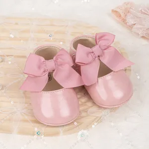 Pink infant princess shoes with oversized bow and matching lace headband on wooden plate