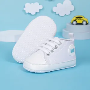 Détail de chaussures bébé en toile blanche avec semelles souples et logo bleu BABY
