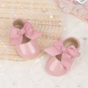 Detailed overhead view of pink pearl PU baby princess shoes with large bow on wooden tray