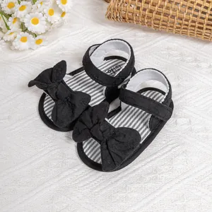 Detailed view of baby girl sandals featuring a large black bow and striped inner sole