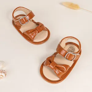 Close-up of brown baby leather sandals with bow decoration and metal buckle detail
