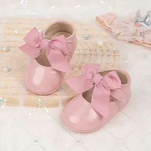 Close-up of pink Mary Jane baby shoes with large grosgrain bows on a lace background