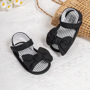 Infant black bow sandals with striped insoles and velcro straps on a white background