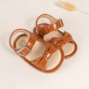 Detail of brown leather baby sandal with bow, buckle strap, and soft stitch texture