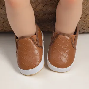 Detailed top view of dark brown woven slip-on baby shoes with white rubber soles on an infant