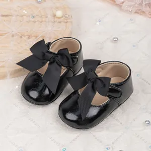 Polished black baby girl princess shoes with large bow and non-slip sole on lace backdrop
