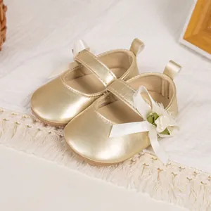 Detail of gold Mary Jane baby shoes featuring silk bow and 3D floral accents