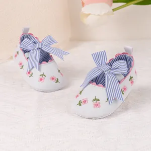 Close-up of baby shoes with pink floral embroidery and blue striped bow decoration