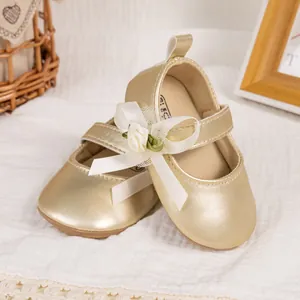 Golden baby Mary Jane shoes with silk bow and floral accent on textured fabric