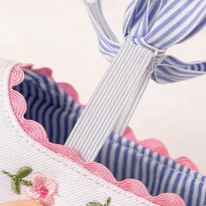 Detail of baby shoes featuring delicate flower embroidery and blue striped bow accents
