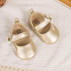Close-up of golden baby Mary Jane shoes with white bow and green flower detail