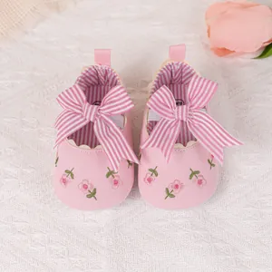 Close-up of pink baby shoes with striped bow, floral embroidery and scalloped edges