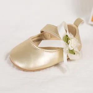 Close-up of golden faux leather baby shoe with a white bow and lace flower detail
