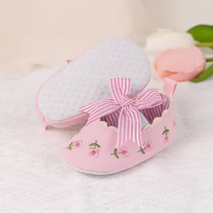 Detail of pink baby shoes with striped bow, floral embroidery and anti-slip soles