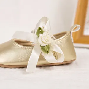 Close-up of baby girl champagne gold shoes with white satin bow and rose flower detail