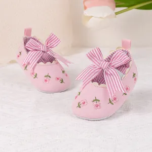 Detail of baby princess shoe with floral embroidery and striped bow on soft cotton fabric