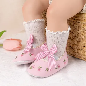 Close-up of pink baby shoes with striped bow and lace socks on cozy carpet