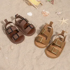 Detail of brown and tan baby sandals with double buckles on a beach sand background