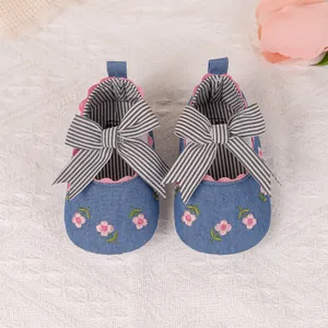 Detailed close-up of blue denim baby shoes with pink flower embroidery and striped bow