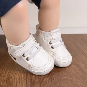 Detail of white leather baby shoes featuring velcro straps and fine stitching on soft soles