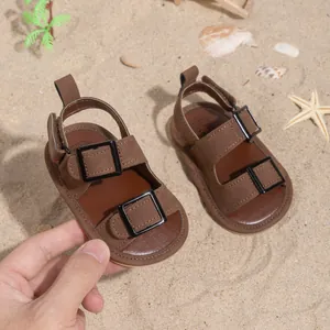Detail of dark brown matte baby sandals with buckle on a summer beach background