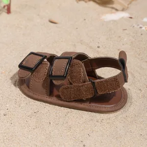Detail of brown baby summer sandals with double buckle straps on a sandy beach background