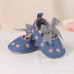 Detail of baby walking shoes with blue denim texture, floral embroidery and striped bow