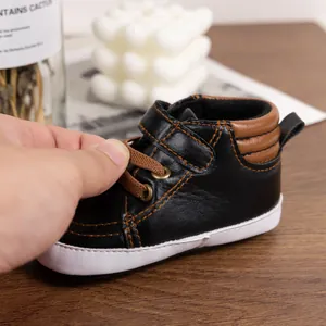 Detail of baby walking shoes with black faux leather, brown laces and hook-and-loop closure
