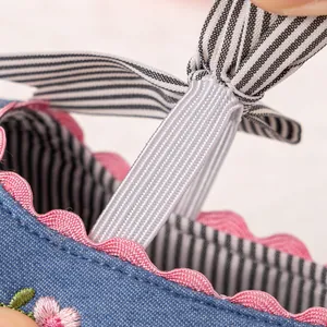 Macro detail showing the elastic striped strap and fine floral embroidery on the baby shoe