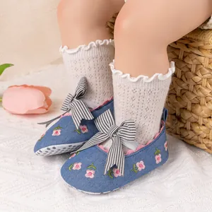 Detailed shot of baby girl denim shoes with floral embroidery and striped bow on white rug