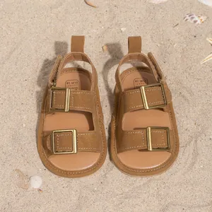 Close-up of brown suede baby sandals with gold buckles on a sunny beach background
