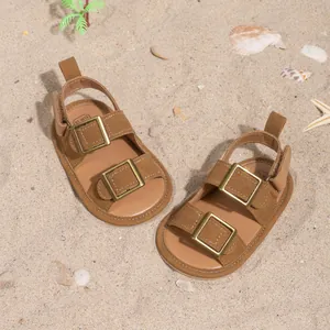 Close-up of brown suede baby sandals with golden buckles on a beach sand background