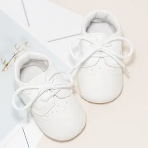 Detailed top view of white leather baby shoes with Brogue style carved floral patterns
