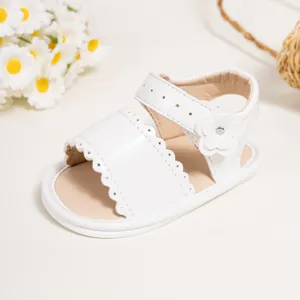 Detail of white infant sandals with scalloped edges and a decorative floral accent