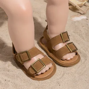 Detail of brown baby sandals with copper buckles on a summer beach background