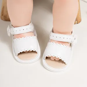 Detail of white baby sandals with scalloped edges and floral accents on wooden background