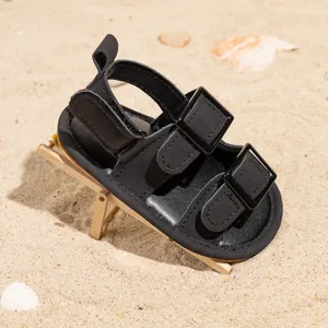 Detail of baby summer walking shoes with double buckle straps and yellow stitching on sand