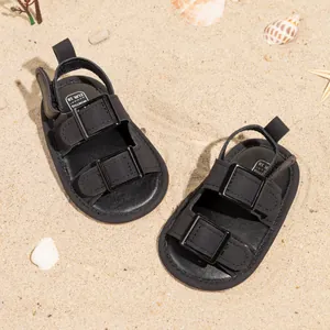 Detail of baby summer sandals in black with adjustable buckle on beach background