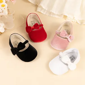 Vue à plat de chaussures de bébé en velours avec nœuds en rouge, rose, noir et blanc