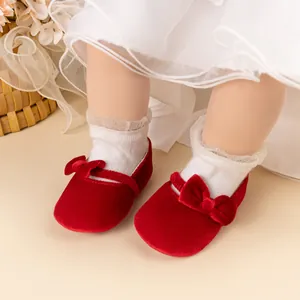 Détail de chaussures bébé en velours rouge avec nœud et chaussettes à dentelle