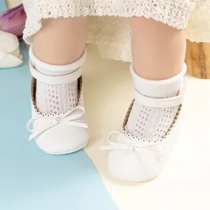 Détail de chaussures de marche bébé Mary Jane blanches avec nœud et bords perforés ondulés