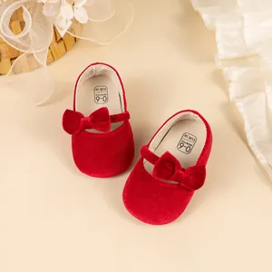 Détail des chaussures bébé Mary Jane en velours rouge avec nœuds sur un tissu crème