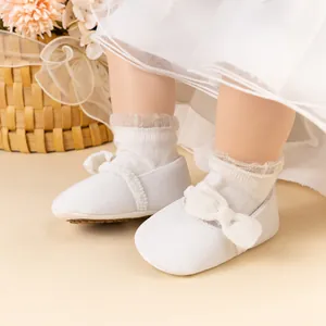 Gros plan de chaussures bébé Mary Jane blanches avec nœud et chaussettes en dentelle
