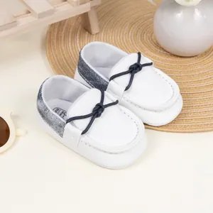 Detail eines weißen Baby-Loafers mit blauer Schleife und Denim-Ferse auf Matte