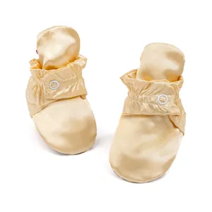 Détail de chaussures bébé en satin doré avec bouton pression et cheville élastique
