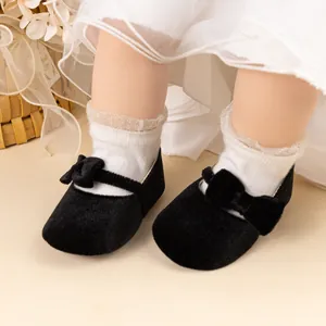 Détail de chaussures bébé en velours noir avec nœud et chaussettes en dentelle