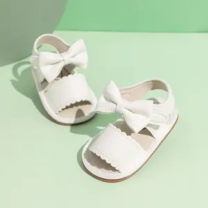 Close-up of white PU leather baby sandals featuring a large bow and scalloped edge detail