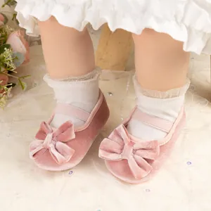 Détail de chaussures bébé en velours rose avec nœud et sangle sur fond de dentelle